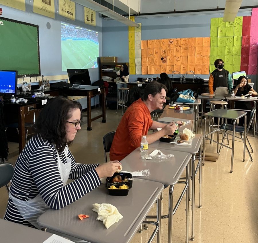 In Mr.Maciass classroom, Mrs.Collins and Mr.Prado are enjoying their Pacegiving food together meanwhile students in the back are eating and watching the World Cup soccer game.